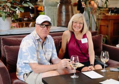 A man and women sitting on a couch drinking wine and looking at the camera